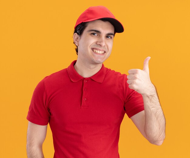 Smiling young caucasian delivery man in blue uniform and cap showing thumb up 