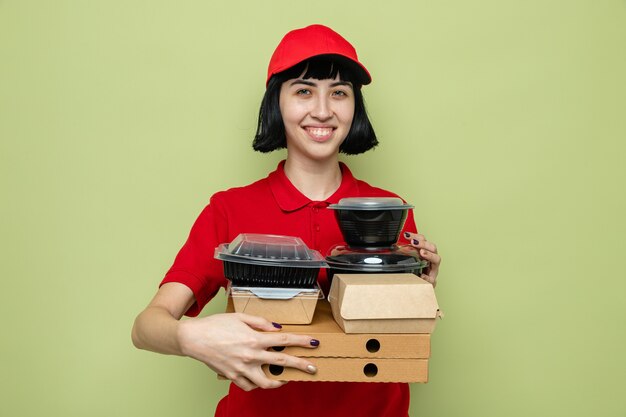 Smiling young caucasian delivery woman holding food containers and pizza boxes