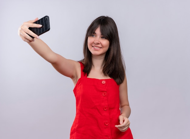 Smiling young caucasian girl holding phone and looking at phone on isolated white background