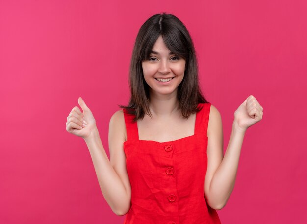 Smiling young caucasian girl holds fists on both hands on isolated pink background
