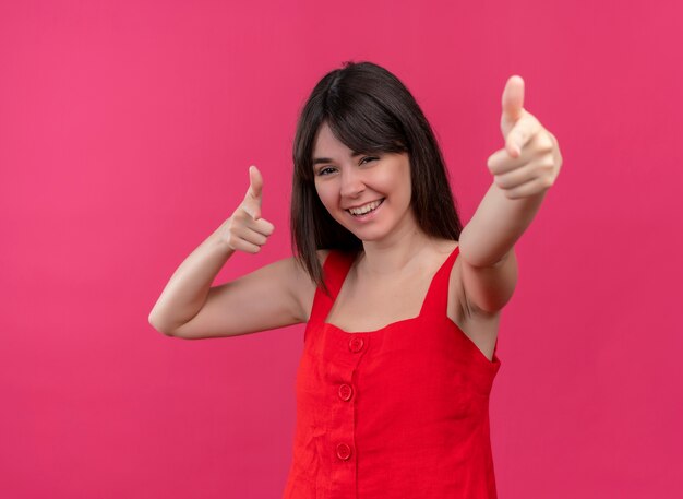 Улыбающаяся молодая кавказская девушка указывая вперед обеими руками на изолированном розовом фоне