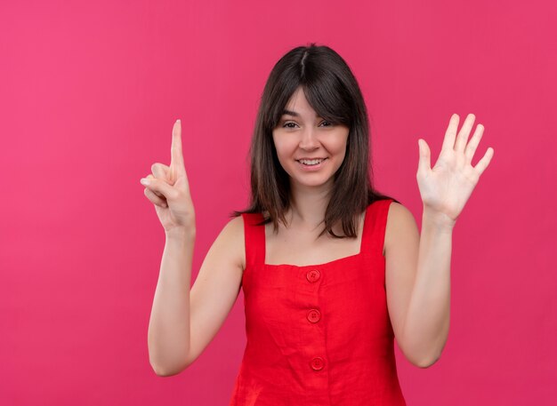 Smiling young caucasian girl points up and holds raises hand on isolated pink background