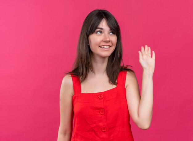 Smiling young caucasian girl raises hand up and looking up on isolated pink background with copy space