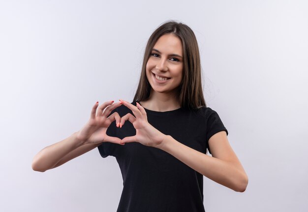 Улыбающаяся молодая кавказская девушка в черной футболке показывает жест сердца на изолированном белом фоне