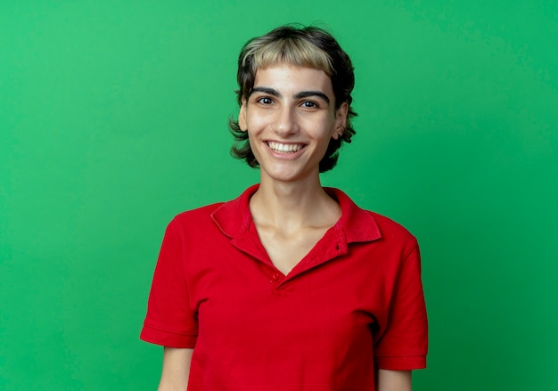 Smiling young caucasian girl with pixie haircut looking at camera isolated on green background with copy space