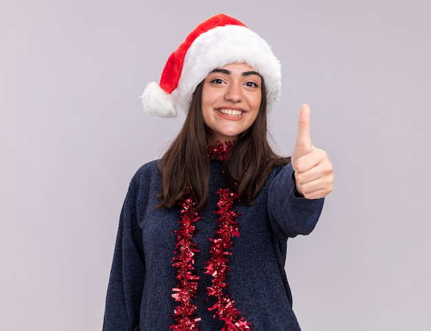 Smiling young caucasian girl with santa hat and garland around neck thumbs up 