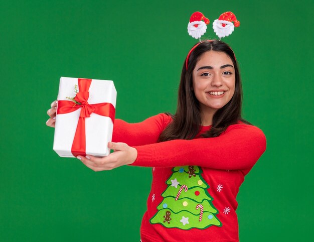 복사 공간 녹색 배경에 고립 된 크리스마스 선물 상자를 들고 산타 머리 띠와 웃는 젊은 백인 여자
