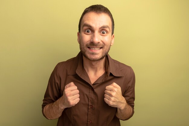 Smiling young caucasian man looking at camera clenching fists isolated on olive green background with copy space