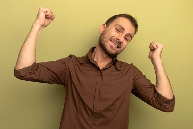 Smiling young caucasian man looking at camera pointing behind isolated on olive green background