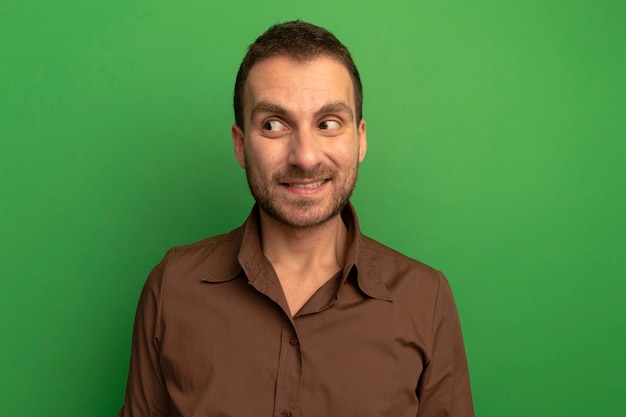 Smiling young caucasian man looking at side isolated on green background with copy space