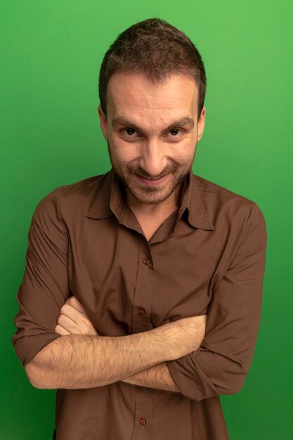 Smiling young caucasian man standing with closed posture  isolated on green wall