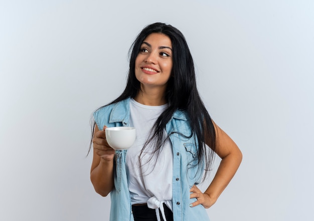 Улыбающаяся молодая кавказская женщина держит чашку, глядя в сторону