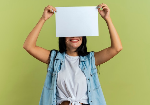 Smiling young caucasian woman holds paper sheet over head closing eyes Free Photo