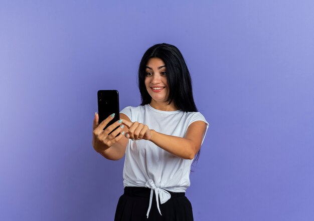 Smiling young caucasian woman looks and points at phone