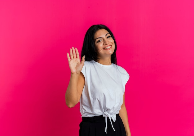 Smiling young caucasian woman stands with raised hand