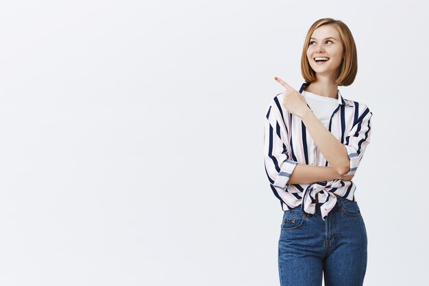 Smiling young confident woman pointing upper left corner at copyspace