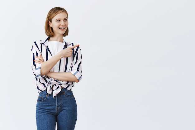 Smiling young confident woman pointing upper right corner at copyspace