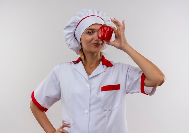 격리 된 흰 벽에 그녀의 손에 후추와 요리사 유니폼 덮여 눈을 입고 웃는 젊은 요리사 여성