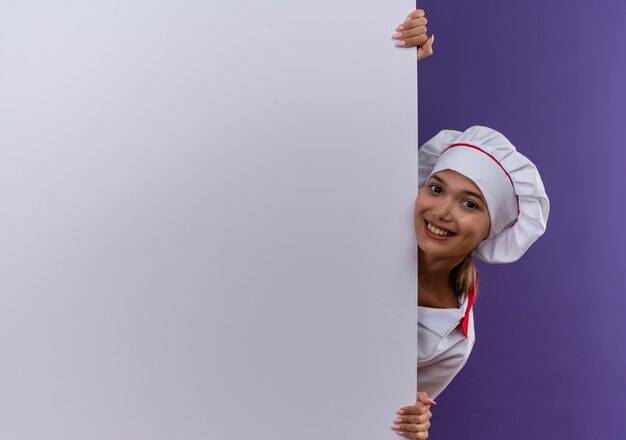 복사 공간 격리 된 배경에 흰 벽을 들고 요리사 유니폼을 입고 젊은 요리사 여성 미소