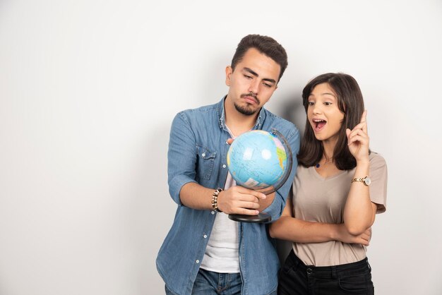 Smiling young couple friends man and woman looking on earth globe.