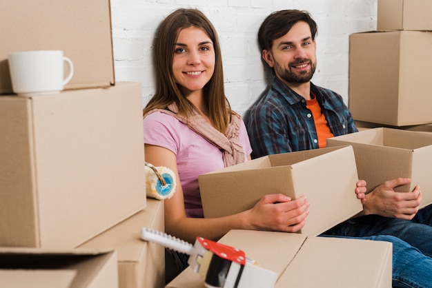 Smiling young couple holding cardboard boxes relaxing in new house