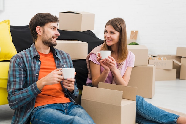 Smiling young couple holding cup of coffee looking at each other with cardboard boxes