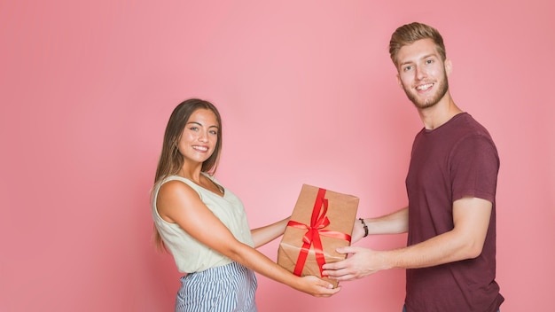 Smiling young couple holding gift box against pink background