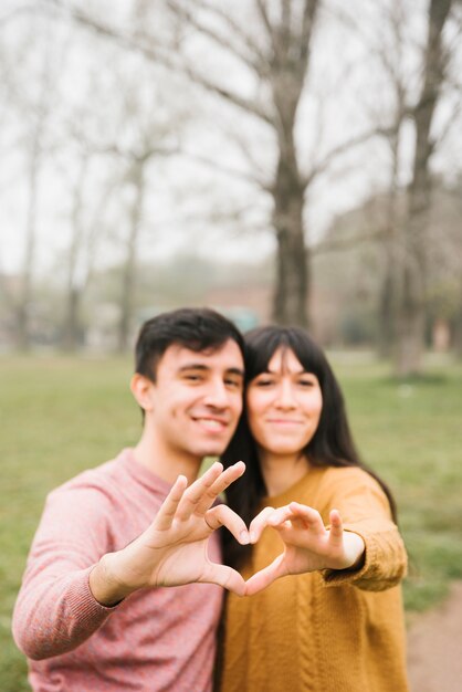 Smiling young couple hugging showing heart gesture