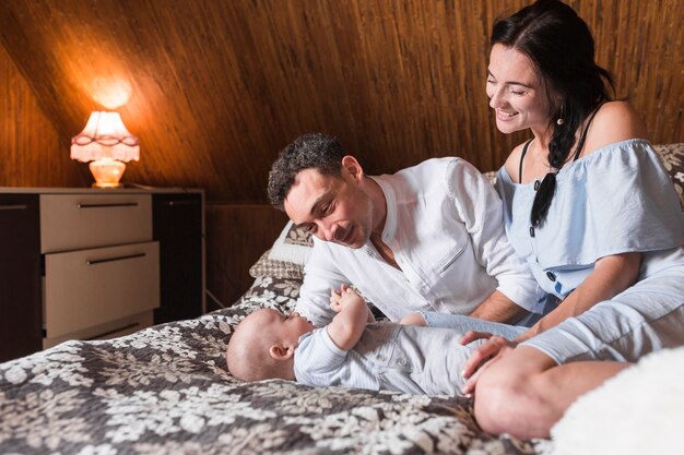 Smiling young couple lying on bed playing with their baby