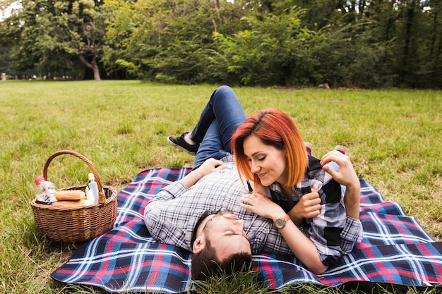 Улыбаясь молодая пара, лежа на одеяло на зеленой траве на пикнике