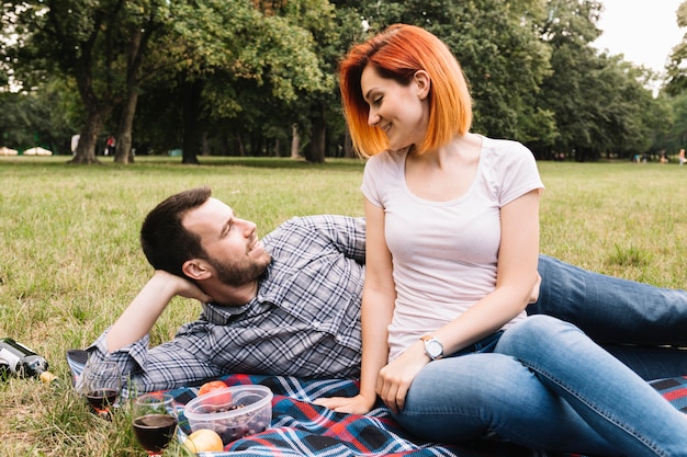 Smiling young couple lying on blanket over green grass with many fruits