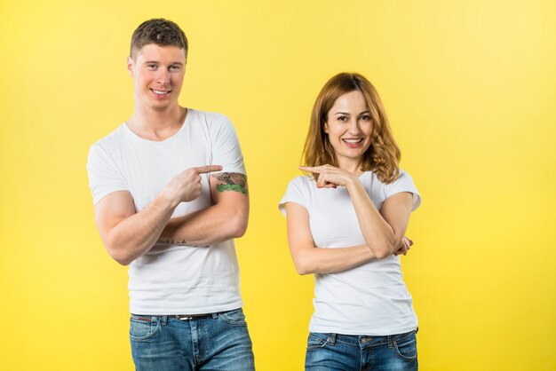 Smiling young couple pointing fingers to each other looking to camera
