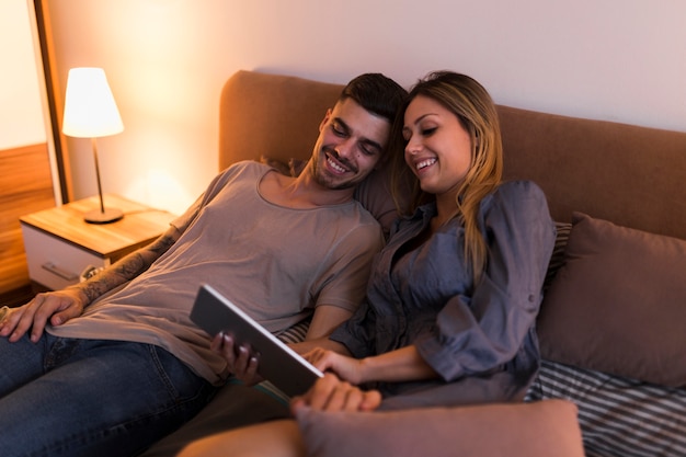 Smiling young couple relaxing on bed using laptop