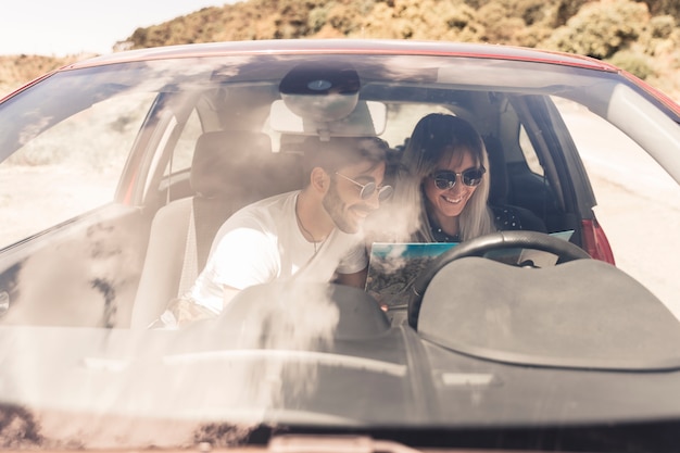 Smiling young couple sitting inside the car looking at map