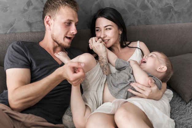 Smiling young couple sitting on sofa playing with his son at home