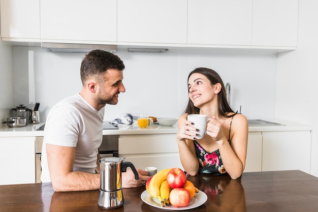 コーヒーを楽しんでキッチンで一緒に座っている若いカップルの笑顔