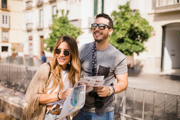 Smiling young couple standing on street holding map