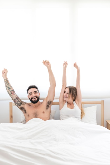 Улыбаясь молодая пара, протягивая руки на кровати