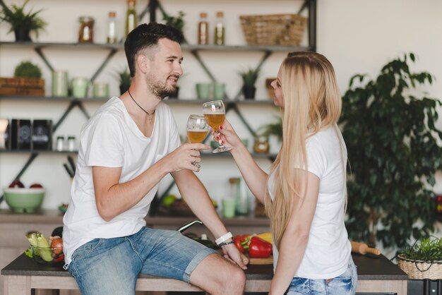 キッチンでビールグラスを焼く若いカップルに笑顔