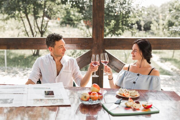 Le giovani coppie sorridenti che tostano i vetri di vino con la mela fruttifica sulla tavola