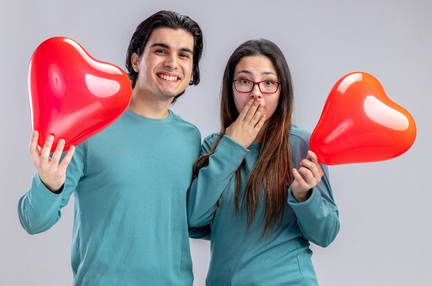 Smiling young couple on valentines day holding heart balloons isolated on white background