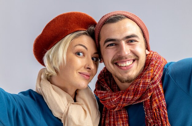 Smiling young couple on valentines day wearing hat with scarf holding camera isolated on white background