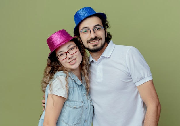 Улыбающаяся молодая пара в розово-голубой шляпе изолирована на оливково-зеленой стене