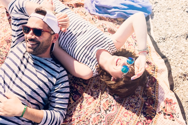 Smiling young couple wearing sunglasses lying on blanket