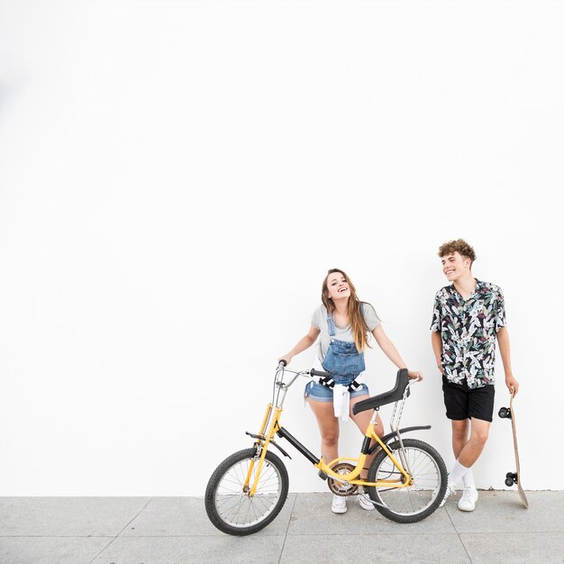 Smiling young couple with bicycle and skateboard against wall