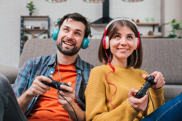ビデオゲームで遊ぶ彼らの頭の上にヘッドフォンと若いカップルの笑顔