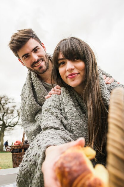 焼かれたクロワッサンを与えるグレーの毛布で包まれた笑顔の若いカップル