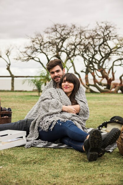 Smiling young couple wrapped in gray blanket sitting in the garden