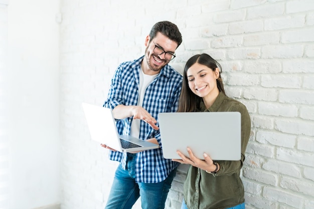 Free photo smiling young coworkers using laptops against white wall in office