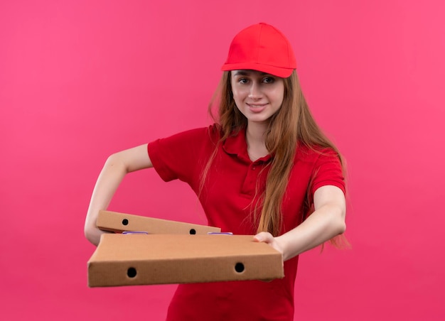 Giovane ragazza sorridente di consegna in uniforme rossa che tiene e che allunga i pacchetti sullo spazio rosa isolato